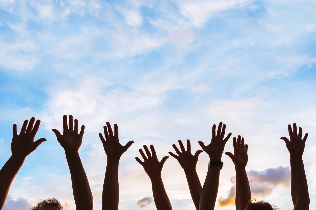 Community members raising their hands together toward the sky